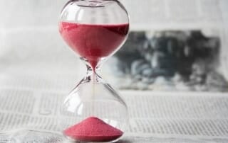 An hour glass with red sands flowing to indicate time passing