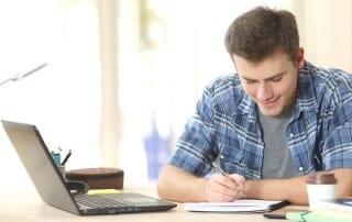 Boy taking notes whilst working with online tutor